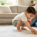 Toddler crouching to pick up a toy while a parent watches in a warm living room