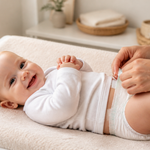 Parent gently changing a smiling baby’s nappy in a warm nursery