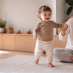 Toddler taking early steps beside a parent in a warm living room